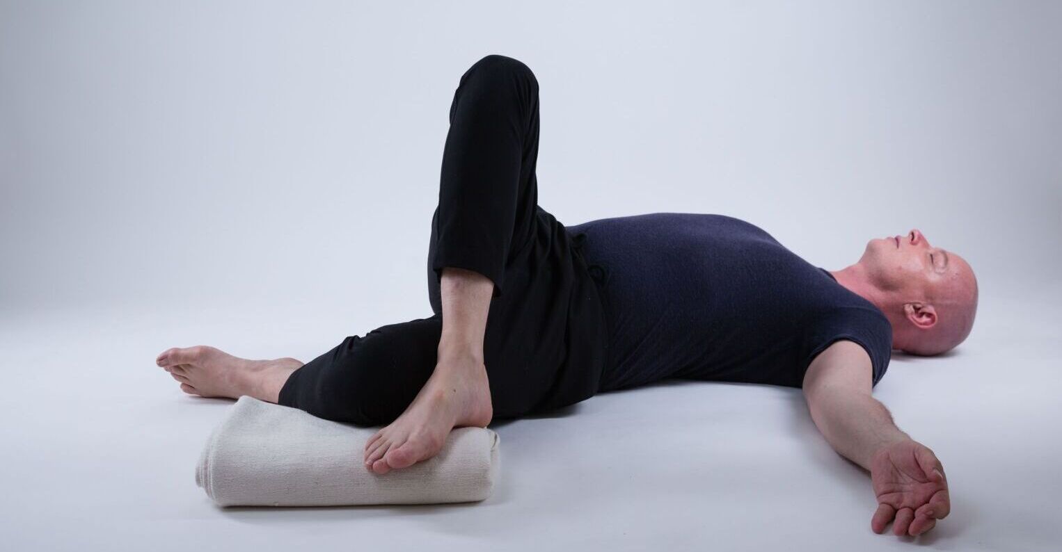 René Hug in Yin Yoga Haltung in Rückenlage mit Unterstützung von Bolstern